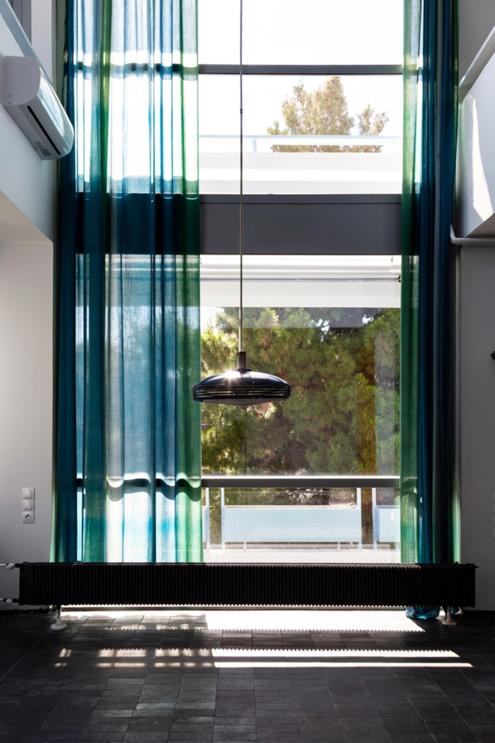 Double-height space with blue-green curtains in the Duplex Residence in Athens