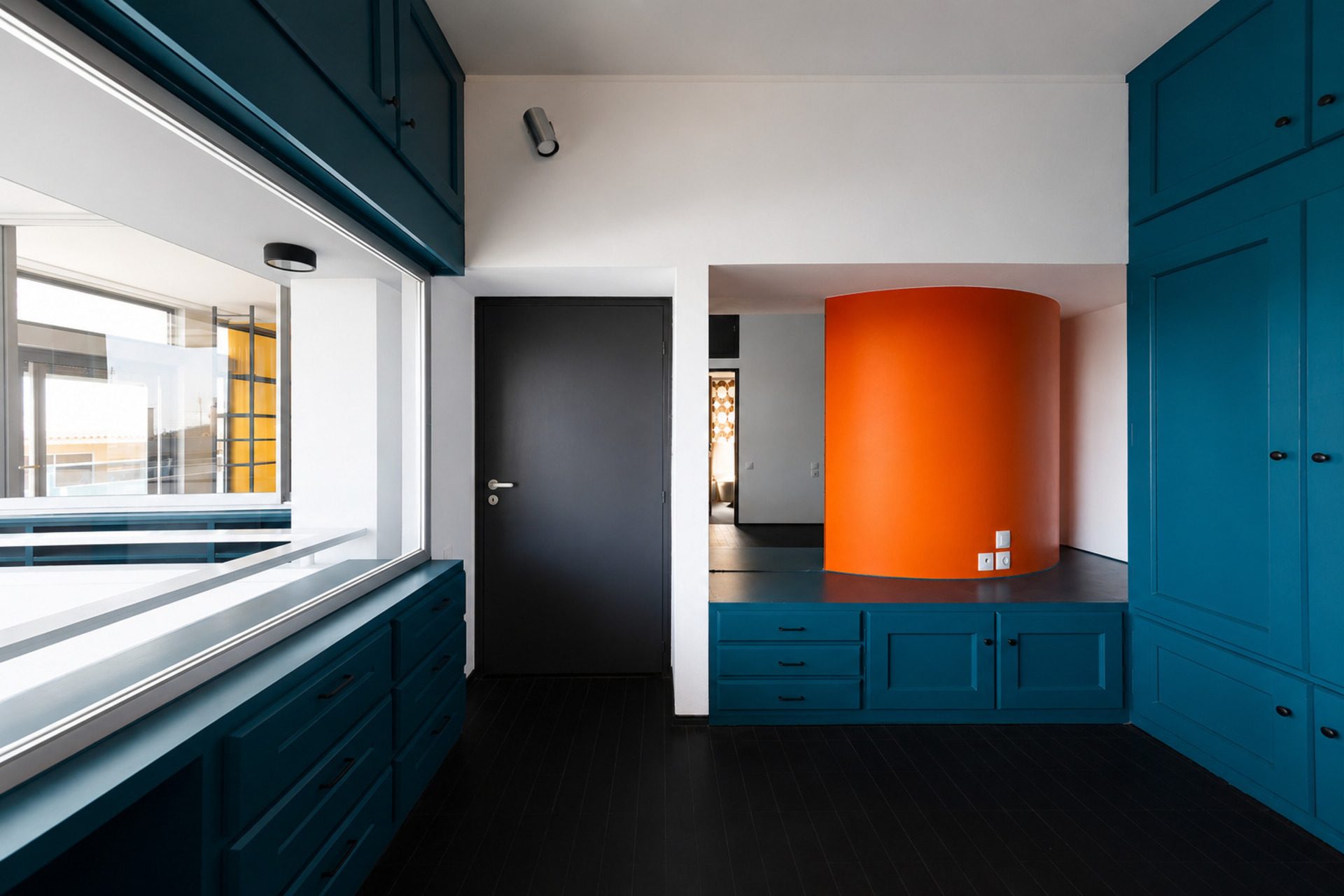 Orange cylindrical stair volume beside petrol-blue cabinetry, Duplex Residence in Athens