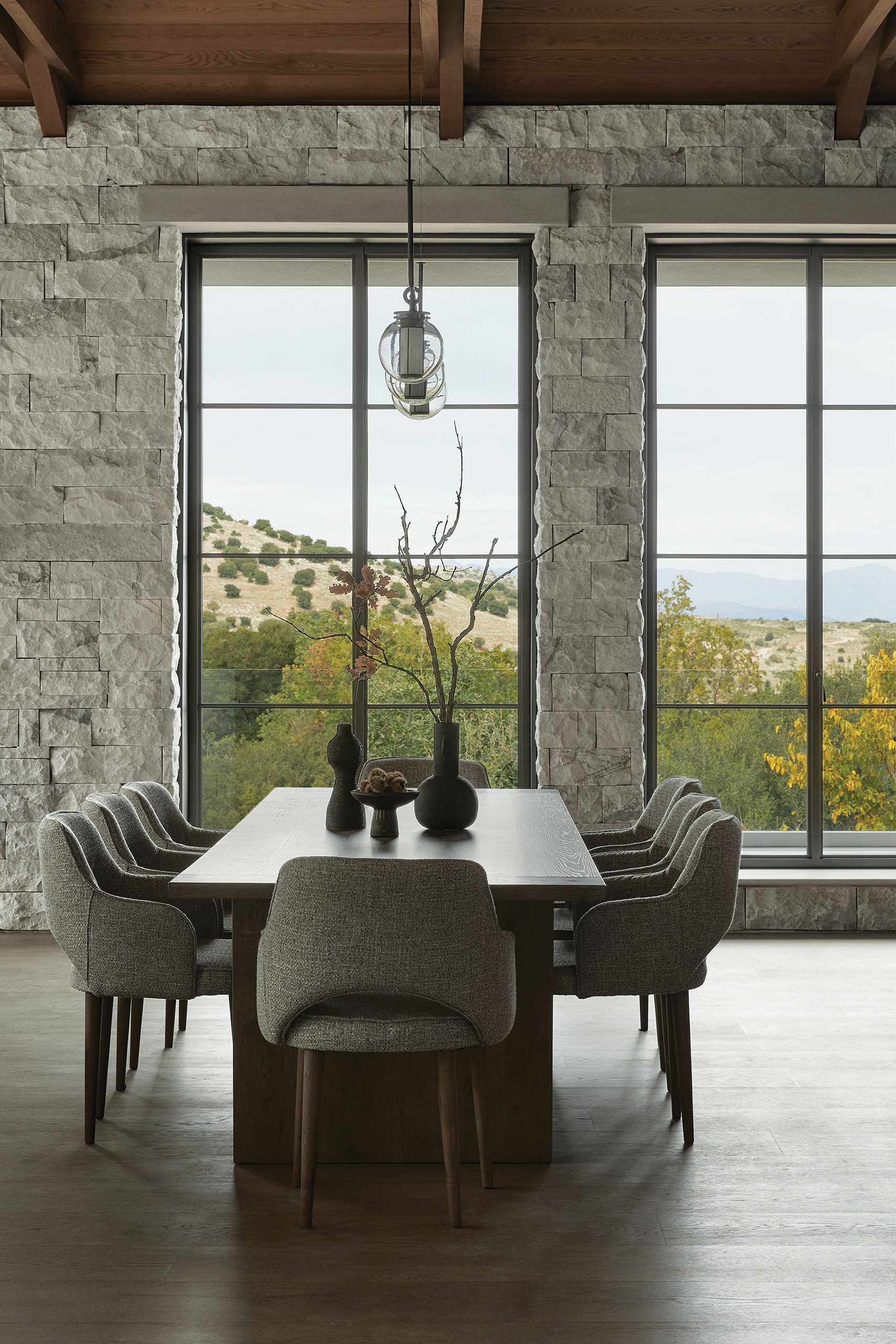 Dining table framed by tall windows and stone wall at Patrion House