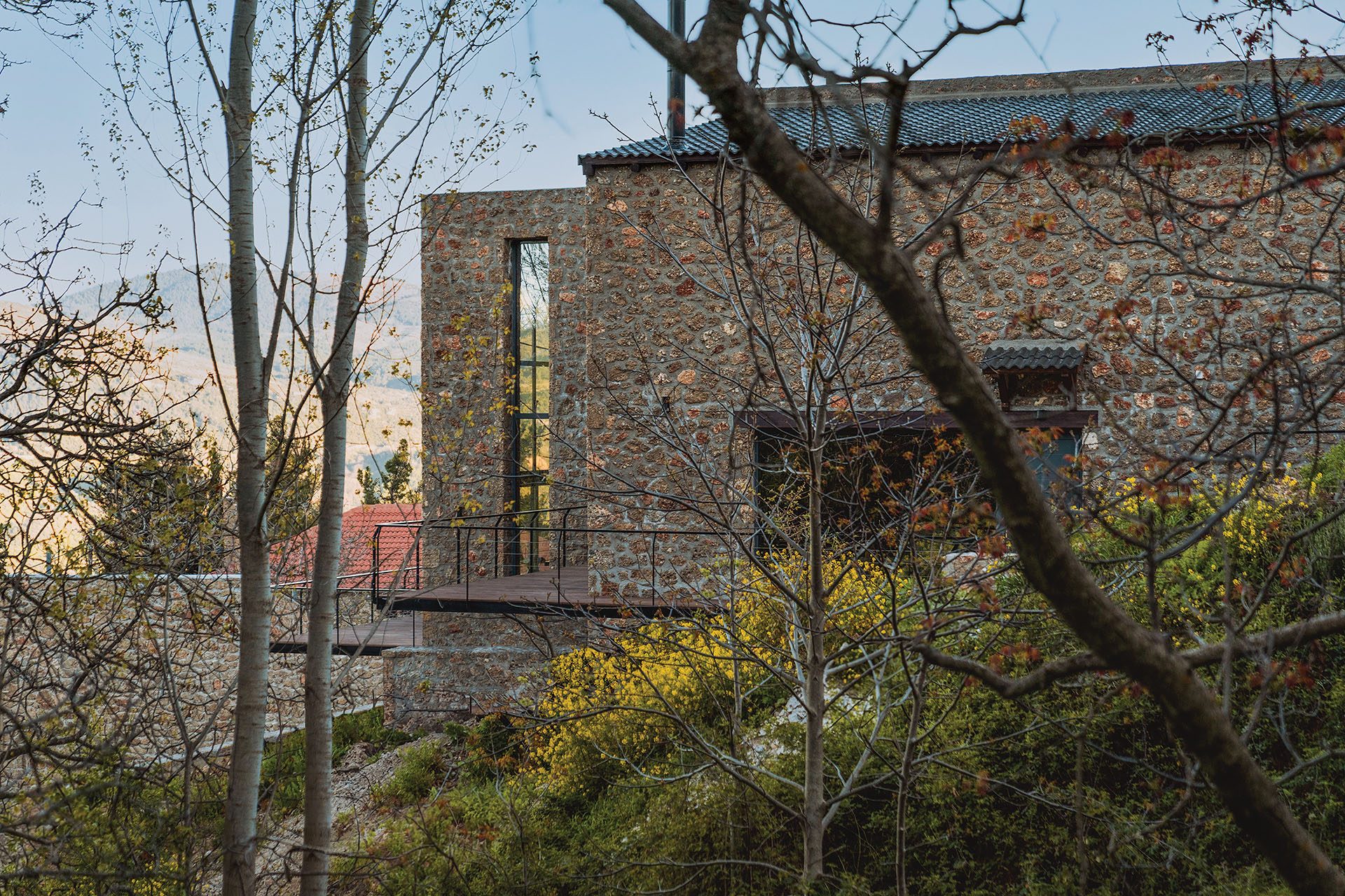 Stone house with pitched tiled roof at Slope seen through trees